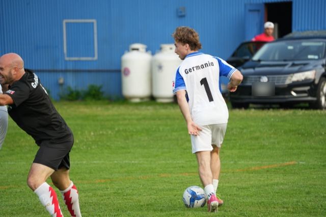 A player in Germania's white and blue number 1 kit brings the ball forward at Germania, June 2025