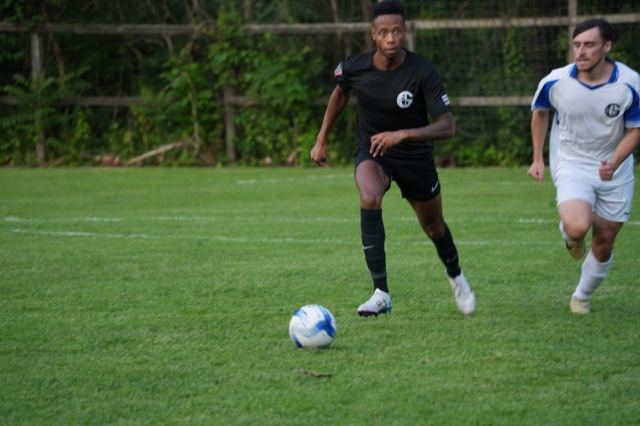 A player in black sprints onto a through ball with a defender in white chasing, June 2025