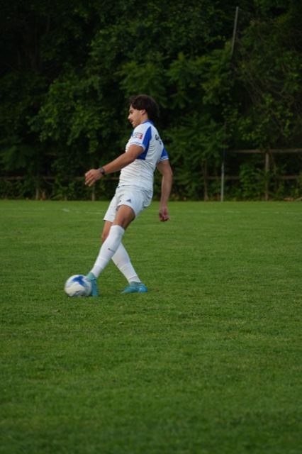 A player in white plays a pass across the grass at Germania, June 2025