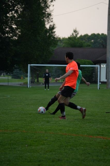 Players in orange and green contest the ball in front of goal, June 2025