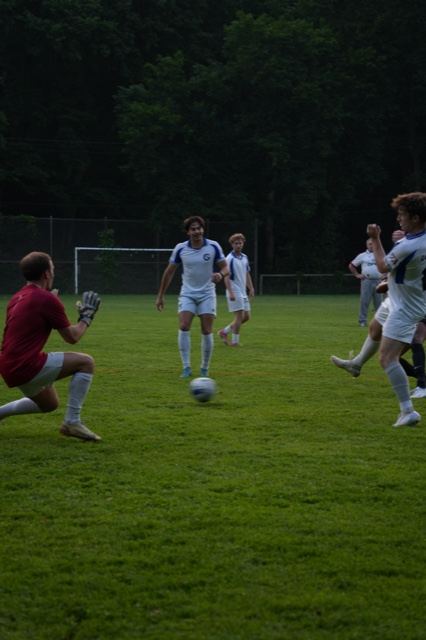 A goalkeeper in red gets down to gather a shot at Germania, June 2025