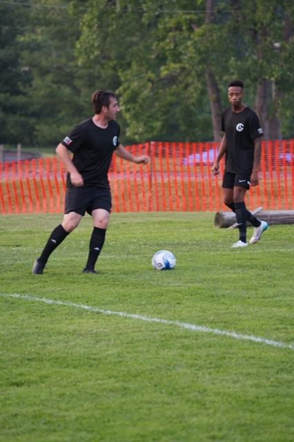 Two teammates in black work the ball near the sideline at Germania, June 2025