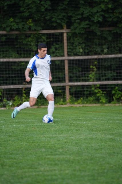 A player in white and blue carries the ball along the fence line at Germania, June 2025
